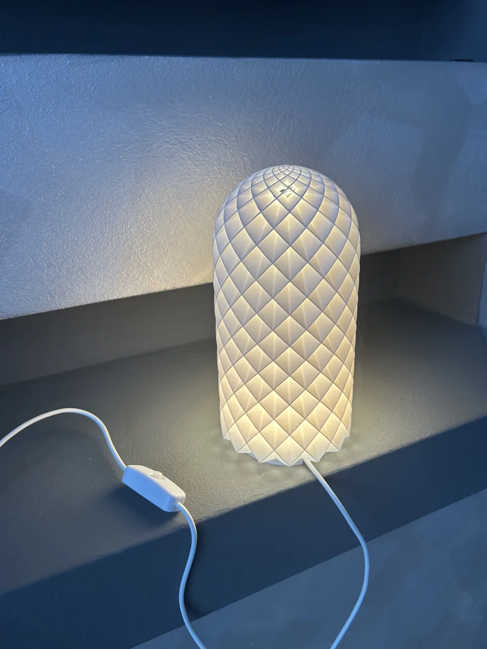 Cilindrična lampa s geometrijskim uzorkom na polici.