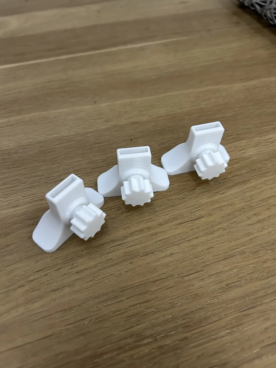 Tri mala bijela 3D printana dijela na drvenoj površini.